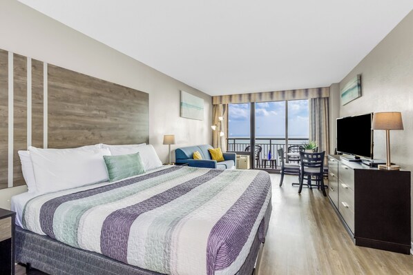 A hotel room with a large bed, a desk with a chair, a TV, and a balcony with a view.