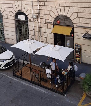 An outdoor cafe with white umbrellas, a stone building, and a parked car. - Centurions Room (Roma)