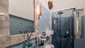 A bathroom with a glass shower enclosure, a white sink, and a mirror with a decorative frame.