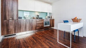 A modern kitchen with wooden cabinets, white countertops, and a white dining table with blue chairs. - 2-bed Apartment Near Basildon Train Station (Basildon)