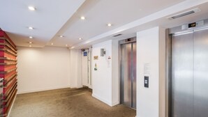 A clean, modern hallway with carpeted floors, white walls, and two elevators. - 2-bed Apartment Near Basildon Train Station (Basildon)