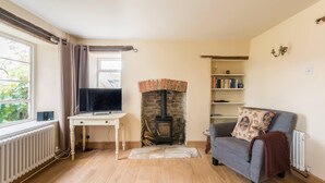 A cozy living room with a fireplace, a television on a wooden table, a grey sofa, and a bookshelf. - Lovely Cosy Stone Cottage in Tetbury, Cotswolds (Tetbury)