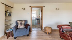 A living room with a sofa, a small side table, a bookshelf, and a wicker ottoman. - Lovely Cosy Stone Cottage in Tetbury, Cotswolds (Tetbury)