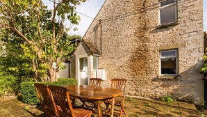 A stone building with a wooden table and chairs in the courtyard. - Lovely Cosy Stone Cottage in Tetbury, Cotswolds (Tetbury)