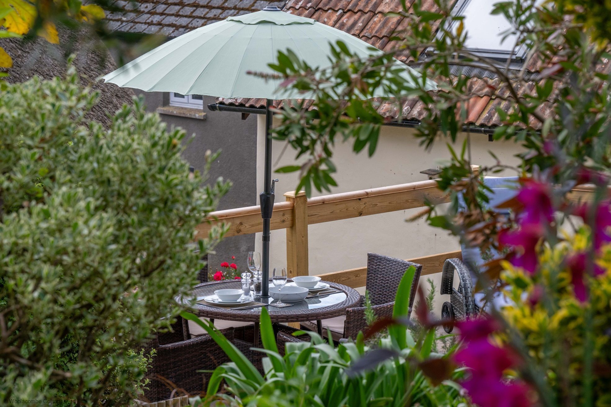 A patio with a table set for two, a green umbrella, and a wooden railing.