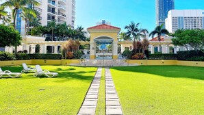 A hotel courtyard with a central fountain, surrounded by palm trees and a pathway leading to the entrance.