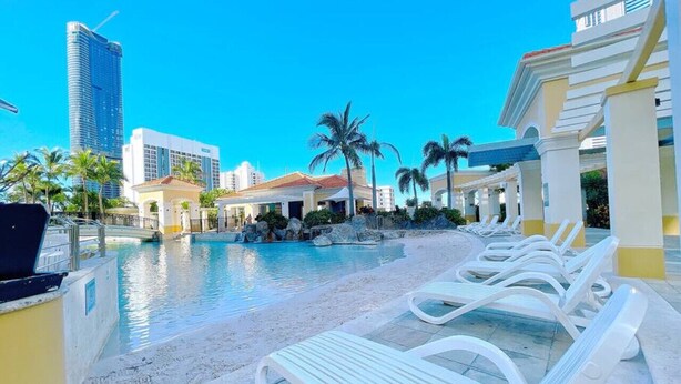 A pool area with lounge chairs, palm trees, and a city skyline in the background.
