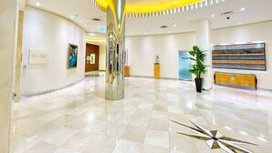 A spacious lobby with a checkered floor, a central metallic column, and a modern ceiling design.