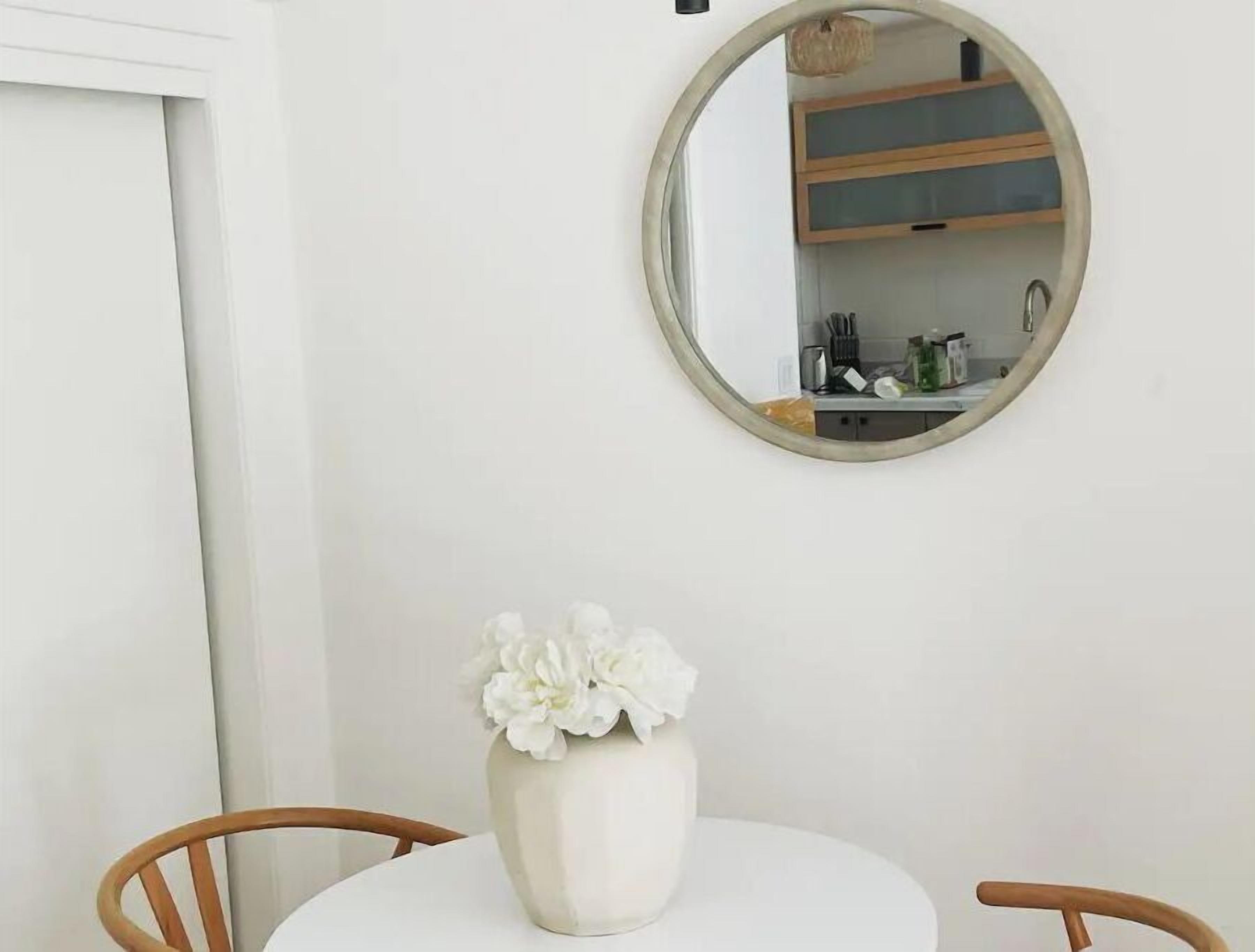 A white dining table with a white vase of flowers, a round mirror on the wall, and wooden chairs. - Luxe modern Lagunitas studio at Samuel P Taylor (Lagunitas-Forest Knolls)