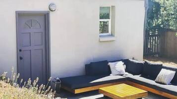 Ein moderner Sitzbereich im Freien mit einer Couch und einem Holztisch, einer Tür und einem kleinen Fenster.