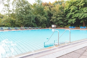 A swimming pool with tiled edges, surrounded by trees and blue chairs.
