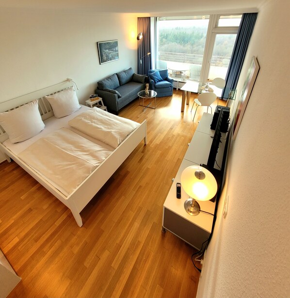 A hotel room with a bed, a sofa, a small table, a lamp, and a TV.