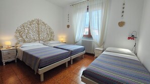 A hotel room with two beds, a decorative headboard, a window with curtains, a radiator, and a wall-mounted light switch.
