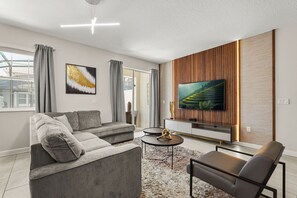 A modern living room with a sofa, a coffee table, a TV, and a large window.