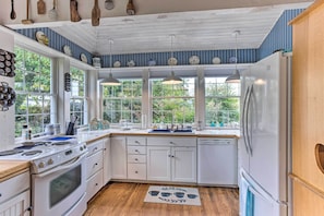 Una cocina con armarios blancos, un refrigerador de acero inoxidable y una ventana con vistas a la vegetación.