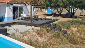 Un área de piscina con una terraza de madera, sillas de descanso y una pérgola.