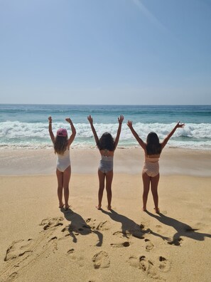 Trois personnes se tiennent sur une plage de sable, le dos tourné vers l’appareil photo, et regardent l’océan.
