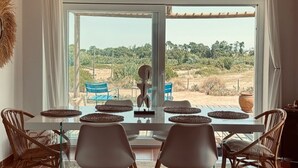 Un comedor con una mesa de vidrio, sillas de mimbre y vistas a un paisaje rural.