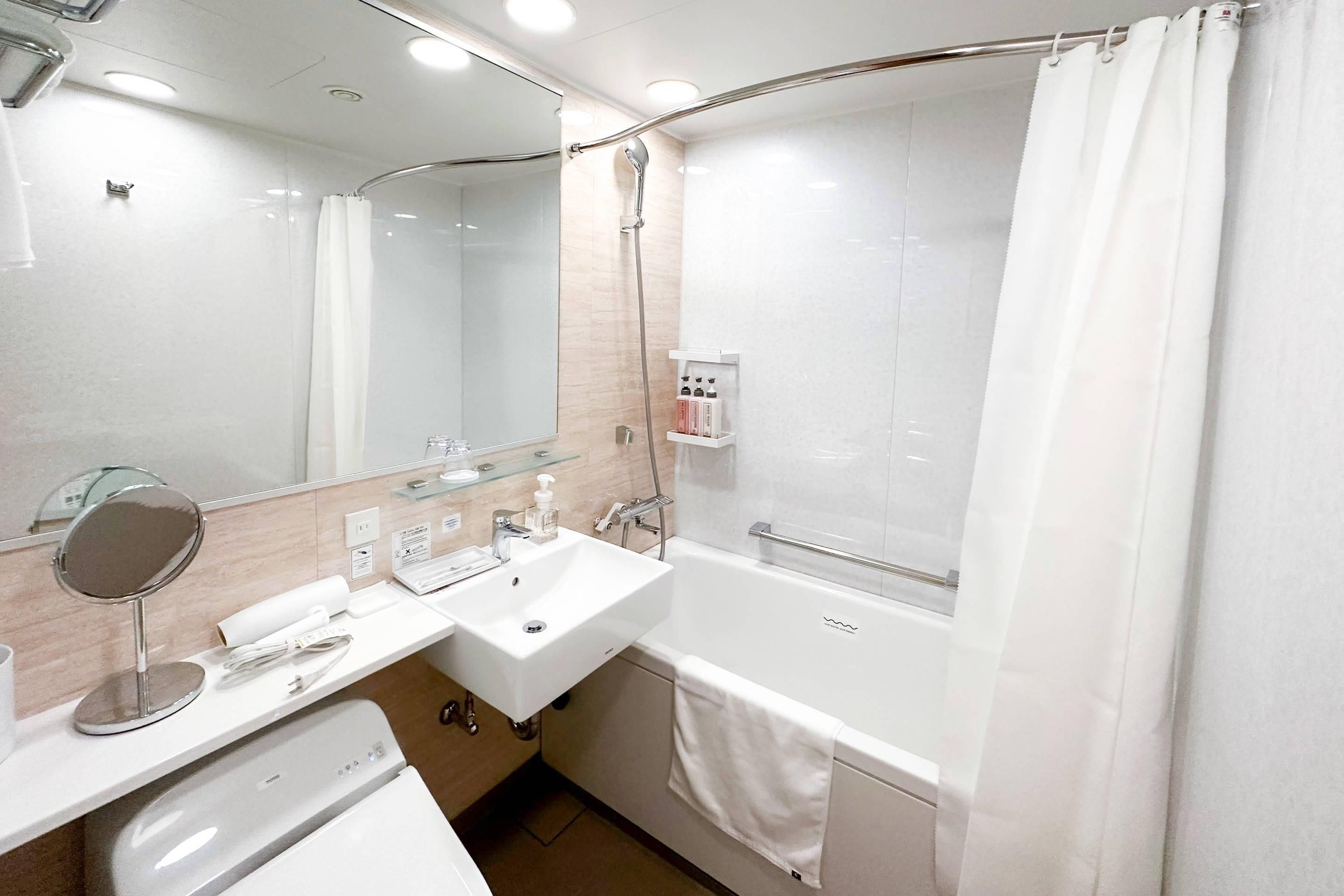 Un baño moderno con lavamanos, espejo y ducha blancos.