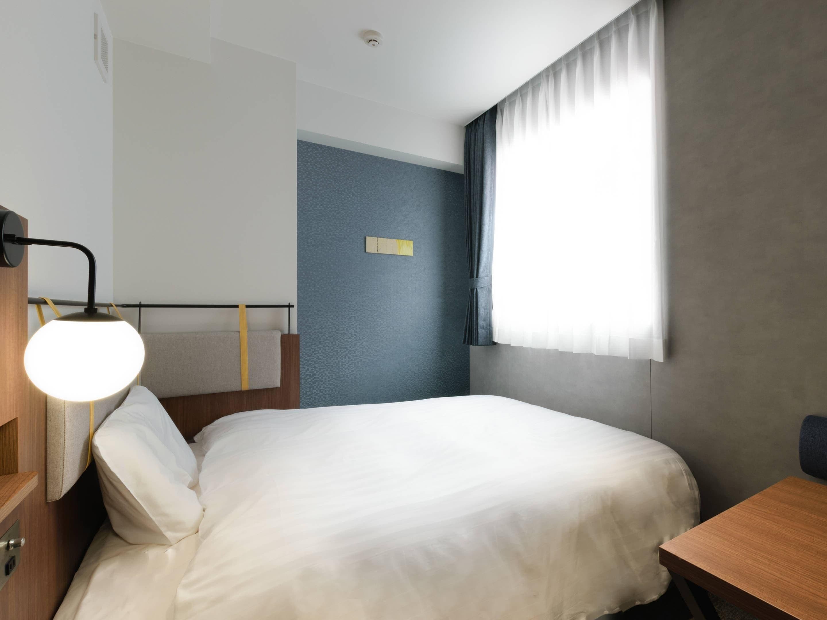 A hotel room with a bed, a bedside table, a lamp, and a window with curtains.