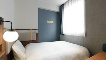A hotel room with a bed, a bedside table, a lamp, and a window with curtains.