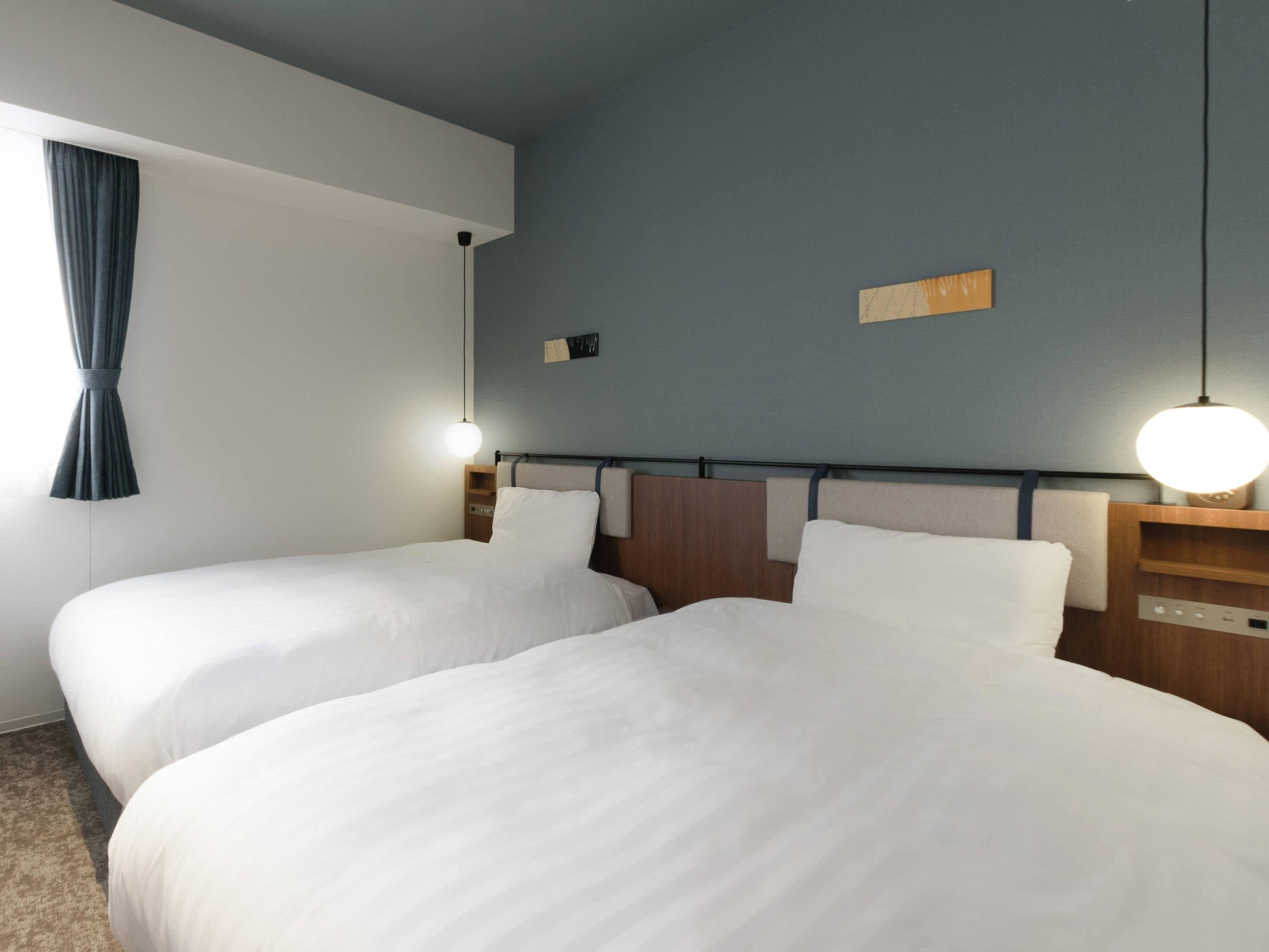 Una habitación de hotel con dos camas, una mesita de noche, una lámpara y un estante en la pared.