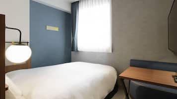 Ein Hotelzimmer mit Bett, Schreibtisch, Stuhl, Lampe und einem Fenster mit Vorhängen.