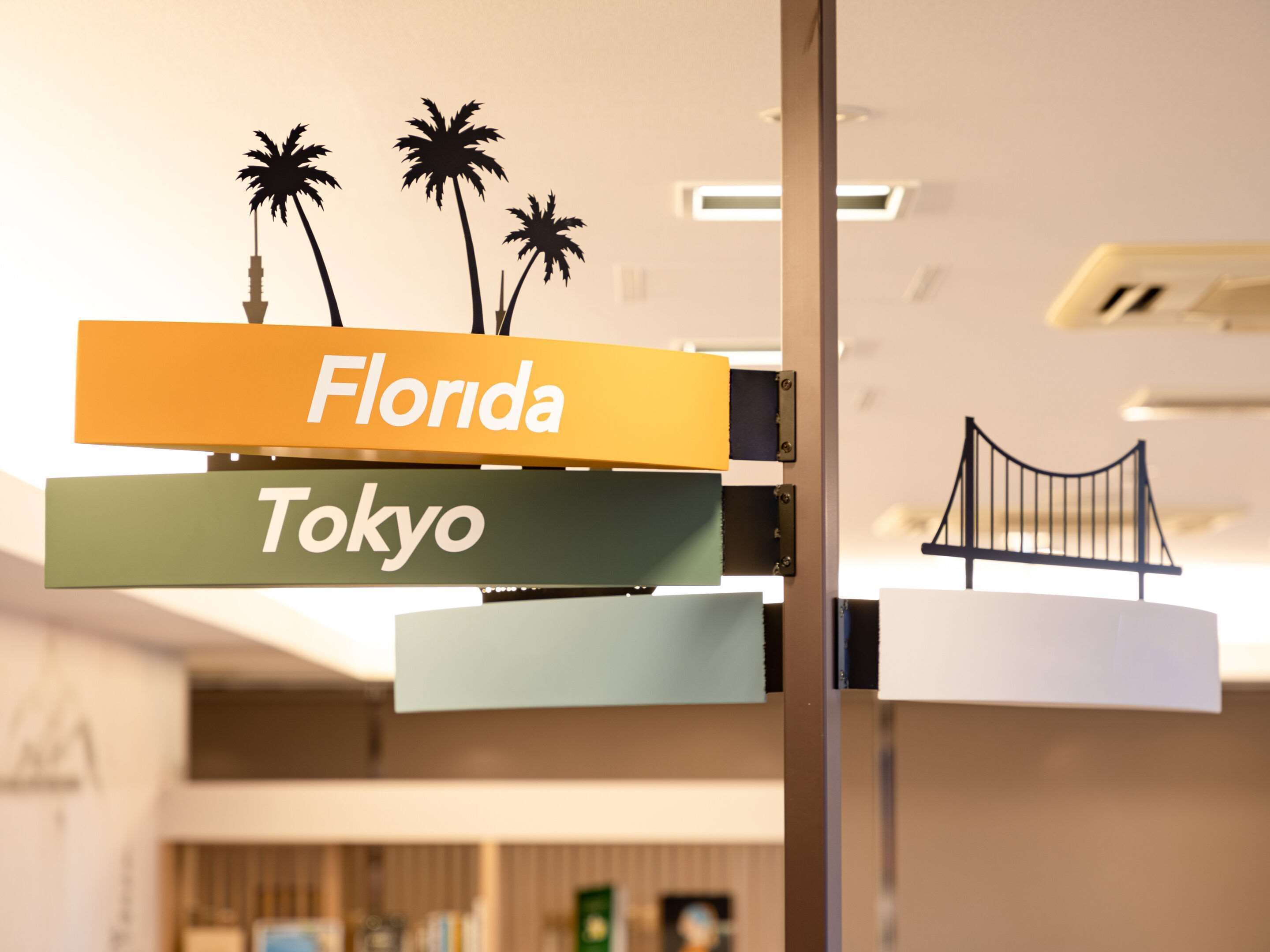 Um letreiro com 'Florida' e 'Tokyo' escrito, com palmeiras e um modelo de ponte acima.