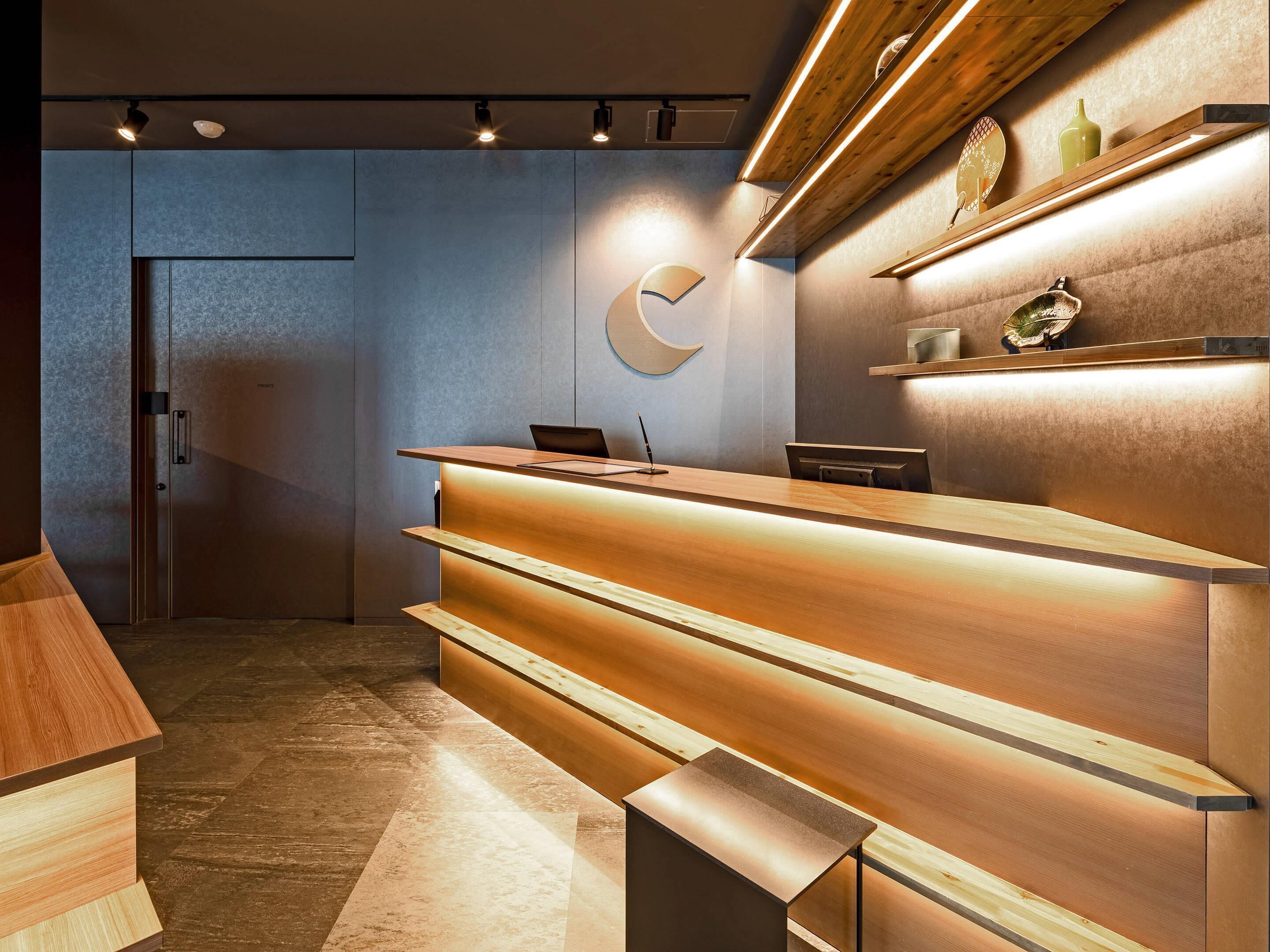 Un moderno mostrador de recepción con iluminación integrada, zona de espera de madera y diseño minimalista.
