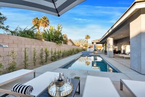 A modern outdoor pool area with a clear view of the pool, a table with a drink tray, and a patio with seating.