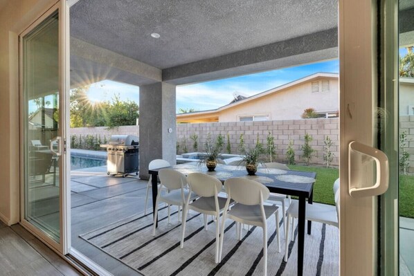 A modern patio with a table and chairs, a grill, and a pool.