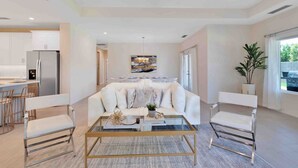 A modern living room with a white sofa, a glass coffee table, and a dining area with a white table and chairs. - Pool/Spa-Location-Basketball-GameRoom-Specials ask (Bermuda Dunes)