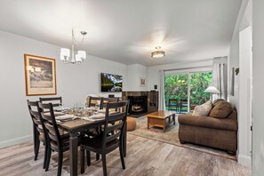 A dining area with a wooden table and chairs, a fireplace, and a sofa in a living room with a view of greenery outside. - Hot Tub|True Ski-In/Ski-Out|Forest View Patio|Managed by Park City Lodging (Park City)