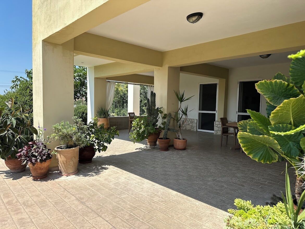 A covered outdoor area with potted plants and a tiled floor.