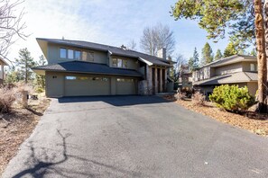 A two-story house with a garage, a driveway, and a small front yard with a tree and shrubs.