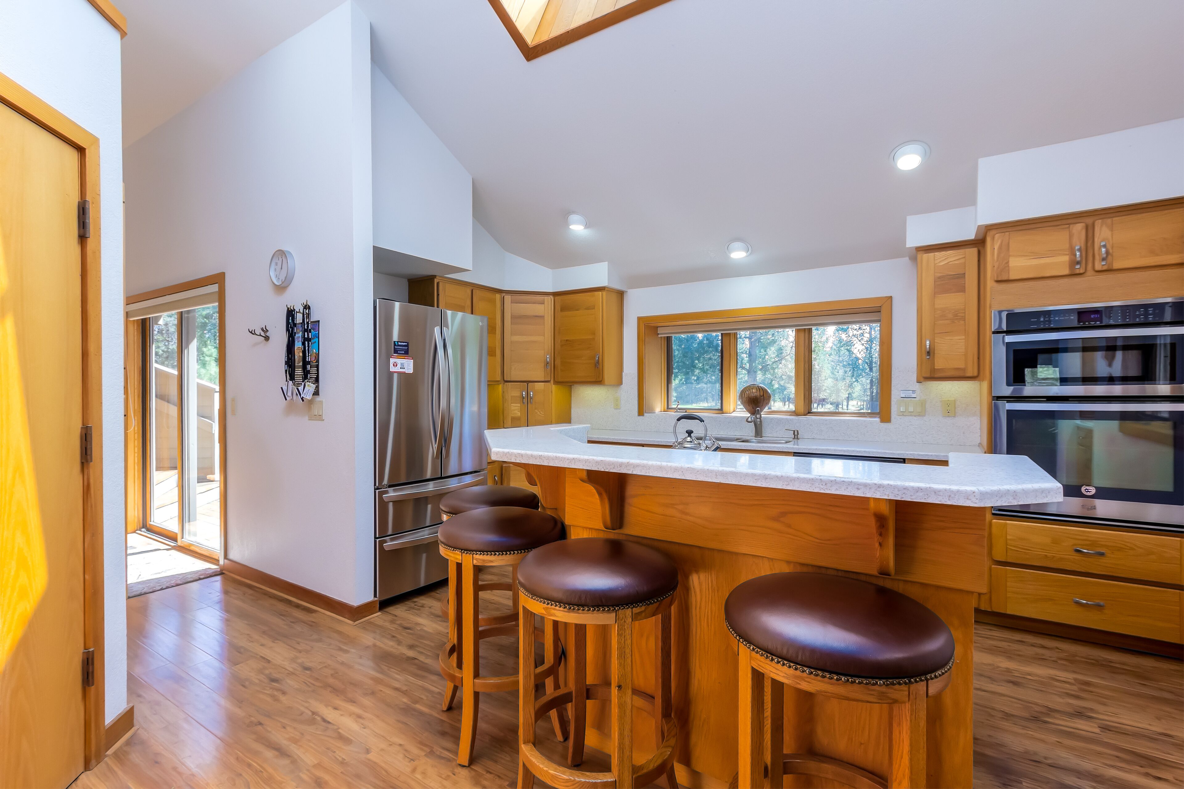 A modern kitchen with wooden cabinets, a stainless steel refrigerator, a large island with stools, and a built-in oven.