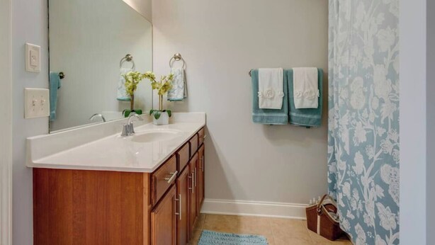 A bathroom with a wooden vanity, a large mirror, and two towels hanging on the wall.