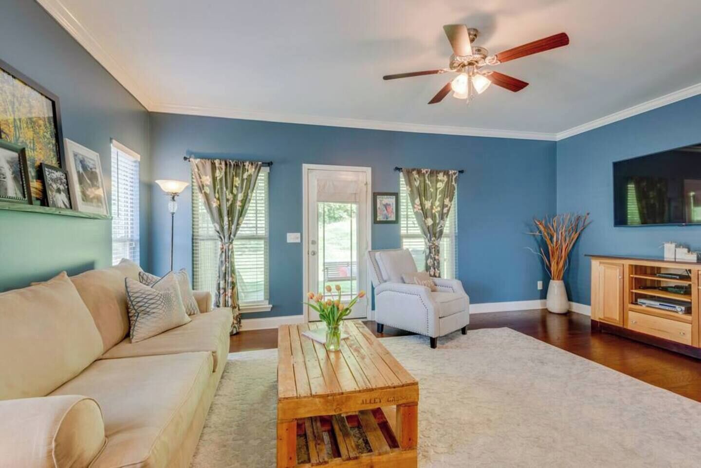 A living room with a beige sofa, a wooden coffee table, a white armchair, and a ceiling fan.