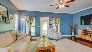 A living room with a beige sofa, a wooden coffee table, a white armchair, and a ceiling fan.
