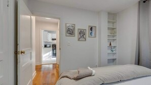 Un dormitorio con cama, una puerta que da a una cocina y una pared blanca con dos cuadros.