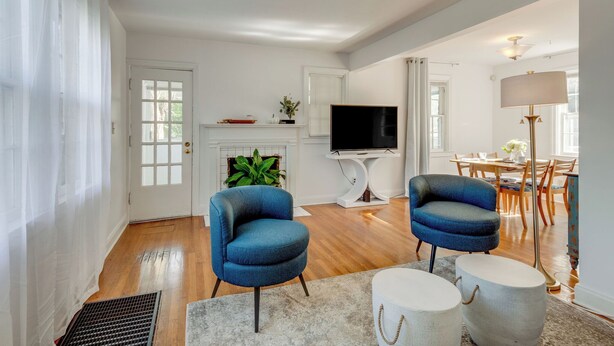 Una sala de estar con dos sillones azules, un televisor de pantalla plana, una chimenea y un comedor con suelo de madera y una mesa preparada para cuatro.