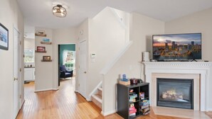 Amplia sala de estar con pisos de madera, chimenea, televisor montado y escalera que conduce a otra habitación.