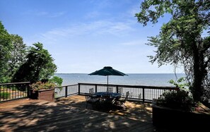 A wooden deck with a table and chairs under a green umbrella, overlooking a body of water. - Spacious 5-Bedroom Waterfront Oasis with Private Dock, Pool and Hot Tub (Tracys Landing)