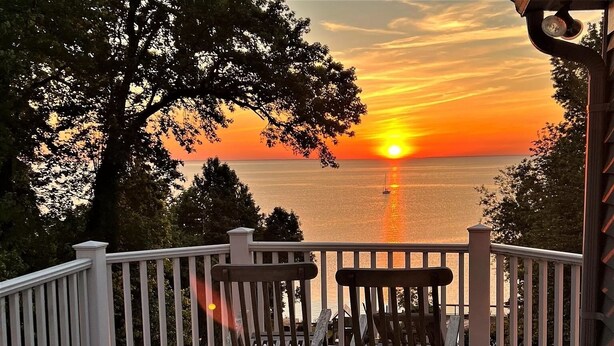 A wooden deck with two wooden chairs facing a sunset over a body of water.