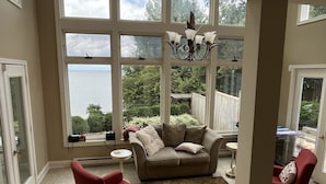 A spacious room with large windows, a chandelier, a sofa, and two armchairs.