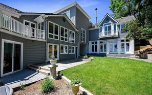 A two-story house with a covered patio, a well-maintained lawn, and a large window overlooking the yard. - Spacious 5-Bedroom Waterfront Oasis with Private Dock, Pool and Hot Tub (Tracys Landing)