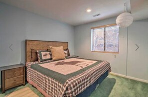 A bedroom with a bed, a nightstand, a window with blinds, and a hanging light fixture.