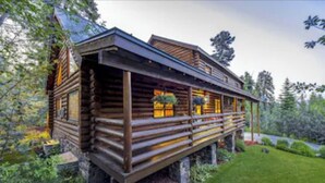 Een vakantiehuisje van hout met een veranda en een stenen fundering, omringd door groen.