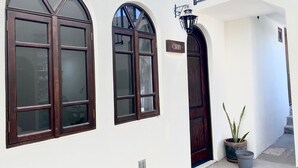 Un edificio blanco con dos grandes ventanales arqueados y una puerta de madera oscura. Se ve un letrero con el nombre 