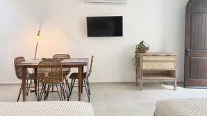 Un comedor con mesa, sillas, un televisor montado y un banco de mimbre.